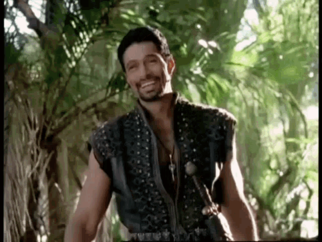 a man with a beard is smiling while standing in the jungle .