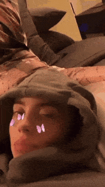 a woman is laying on a bed with butterflies on her face and a hoodie on her head .