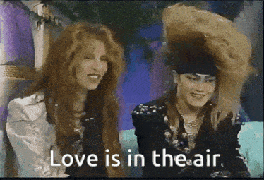 two women are sitting next to each other with the words love is in the air
