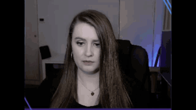 a woman with long hair and a red necklace is sitting in front of a computer screen .