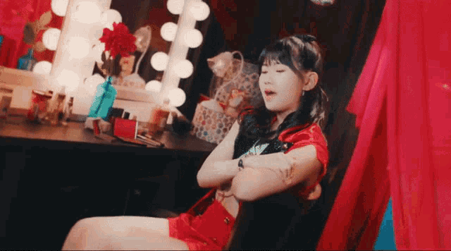 a woman in a red dress is sitting in front of a vanity