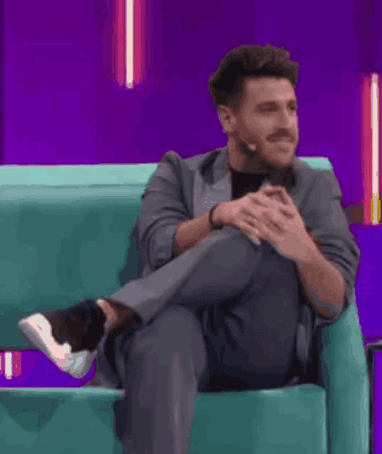 a man in a suit is sitting in a chair with his legs crossed and a microphone .
