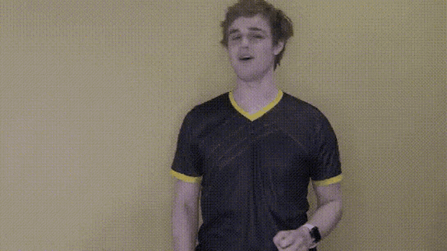 a man in a black shirt with a yellow stripe on the sleeves is dancing against a yellow wall .