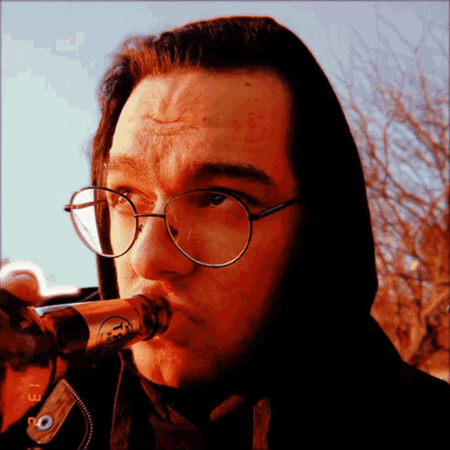 a man wearing glasses and a hoodie drinks from a bottle that says ' 1st ' on it