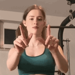 a woman in a green sports bra is making a peace sign with her fingers .