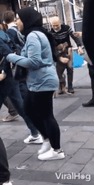 a woman in a hijab is standing on a sidewalk next to a man in a sweater .