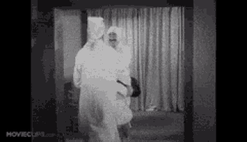 a black and white photo of a man in a white robe standing in a room .