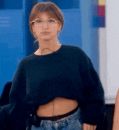 a woman wearing glasses and a black crop top is standing in a room .
