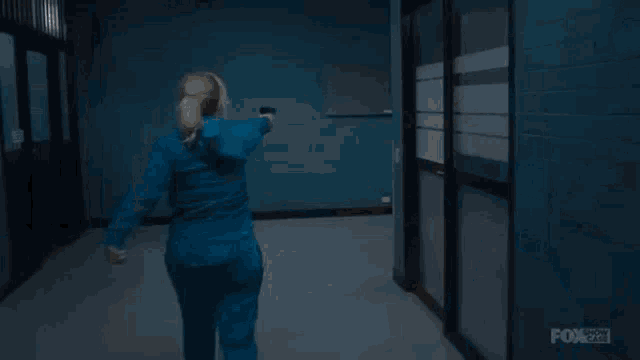 a woman in a blue jacket is standing in a dark room and looking at the camera .