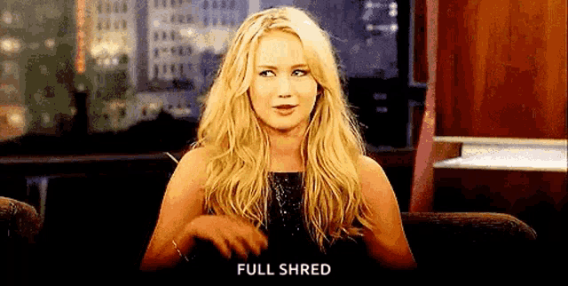 a woman in a black dress is sitting in a chair with her hands in her pockets and says `` full shred '' .
