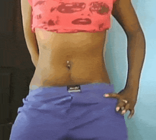 a woman wearing purple shorts and a pink crop top has a piercing in her belly