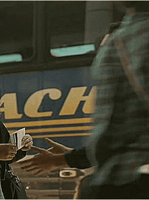 a man in a black hoodie is holding a woman 's hand in front of a bus with the letter a on it .