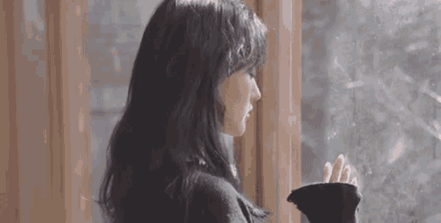 a woman is looking out of a window while holding a cup of coffee .