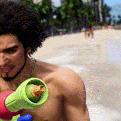 a shirtless man is holding a green water gun on a beach .