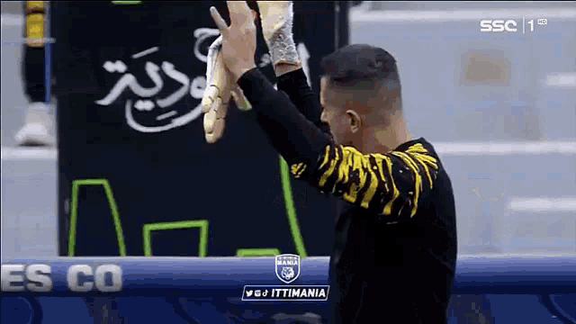a man in a black and yellow shirt is holding a pair of gloves over his head .