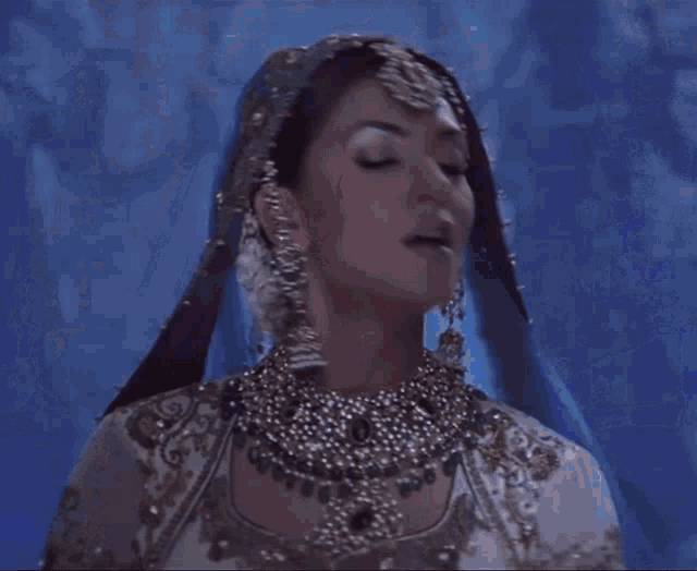a woman wearing a blue veil and gold jewelry is looking at the camera