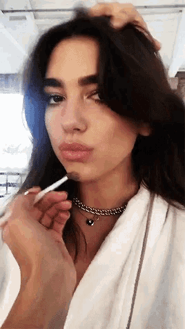 a woman wearing a white robe is applying lip gloss to her lips
