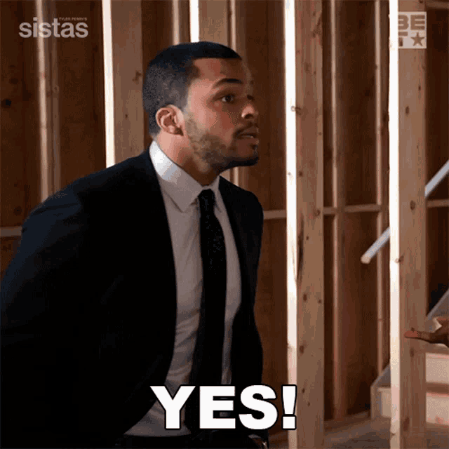 a man in a suit and tie says yes in front of a wooden wall