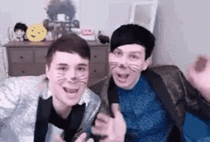 two men wearing cat masks are sitting next to each other on a couch and smiling .