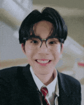a young man wearing glasses and a suit is smiling for the camera .