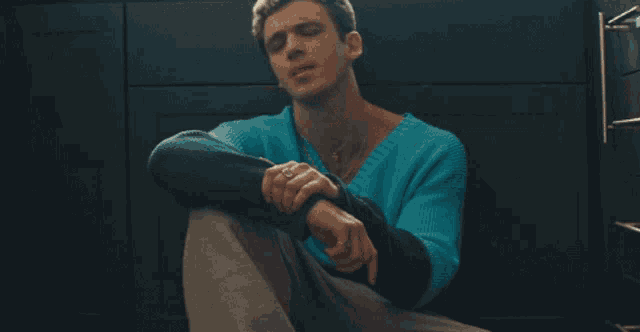 a man in a blue sweater is sitting on the floor