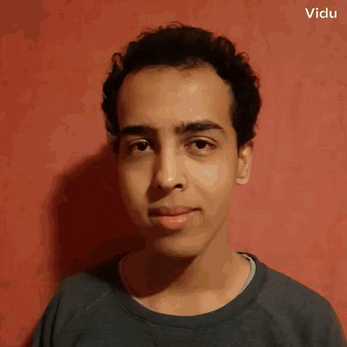 a young man with curly hair is standing in front of a red wall and looking at the camera .
