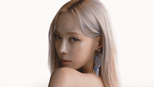 a woman with blonde hair and earrings is looking over her shoulder at the camera on a white background .