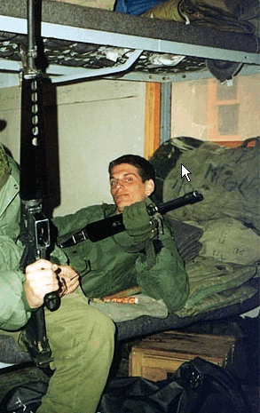 a man laying on a bed holding a gun with a bag that says krause on it