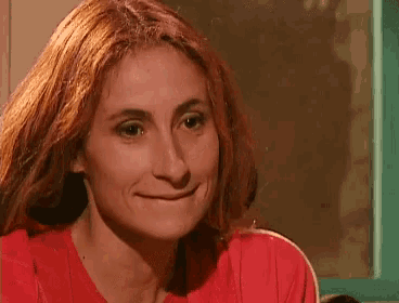 a woman with long red hair is smiling and wearing a red shirt