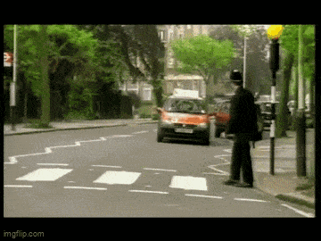 a man in a top hat stands on the side of a road waiting for a car to pass
