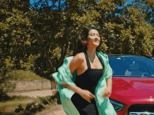 a woman in a black dress is running in front of a red ford mustang