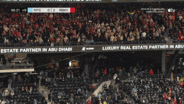 a crowd of people in a stadium watching a game between nyc and rbny with advertisements for partners in abu dhabi