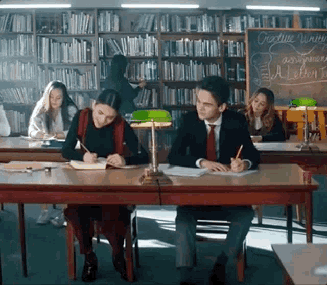 a group of people are sitting at desks in front of a blackboard that says creative writing