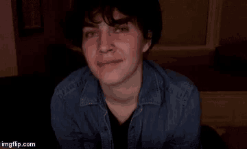a young man wearing a denim jacket and a black shirt is smiling and looking at the camera .