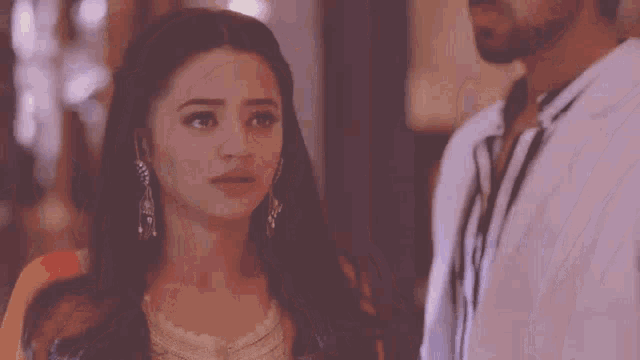 a man and a woman are standing next to each other and looking at each other . the woman is wearing earrings .