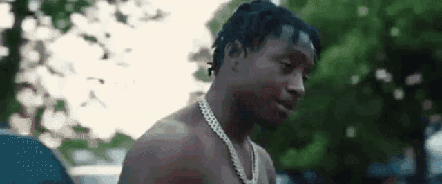 a shirtless man wearing a necklace is standing in front of a car .