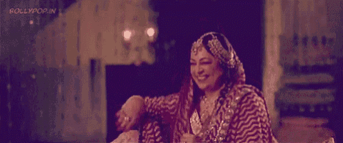 a woman in a traditional indian dress is sitting on a bed and smiling .