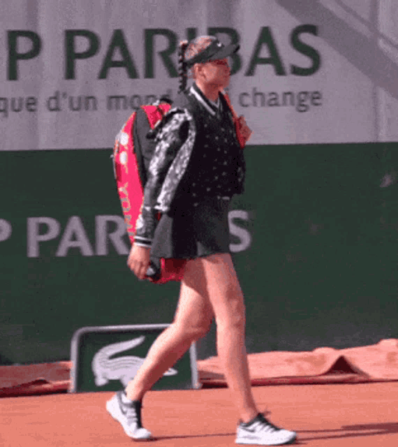 a woman is walking on a tennis court in front of a p parbas banner