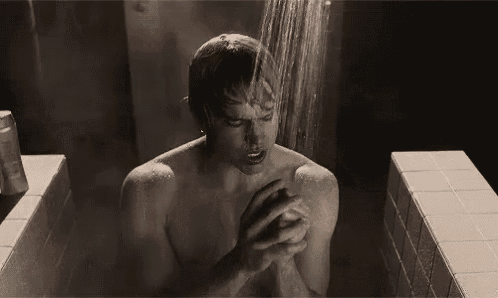 a shirtless man is taking a shower in a bathtub in a black and white photo .