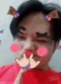 a man wearing a red shirt and ears is making a funny face with his hands on his chin .