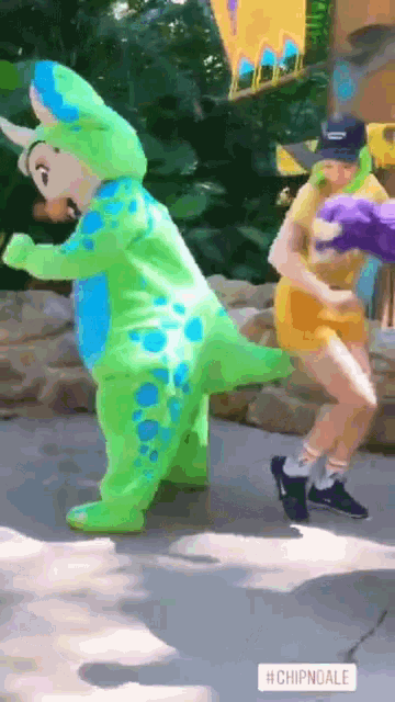 a person in a green and blue dinosaur costume is dancing with another person