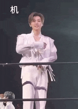 a man in a white suit is standing next to a fence on a stage .