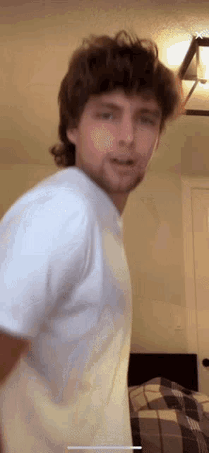 a man in a white shirt is standing in front of a bed in a bedroom .