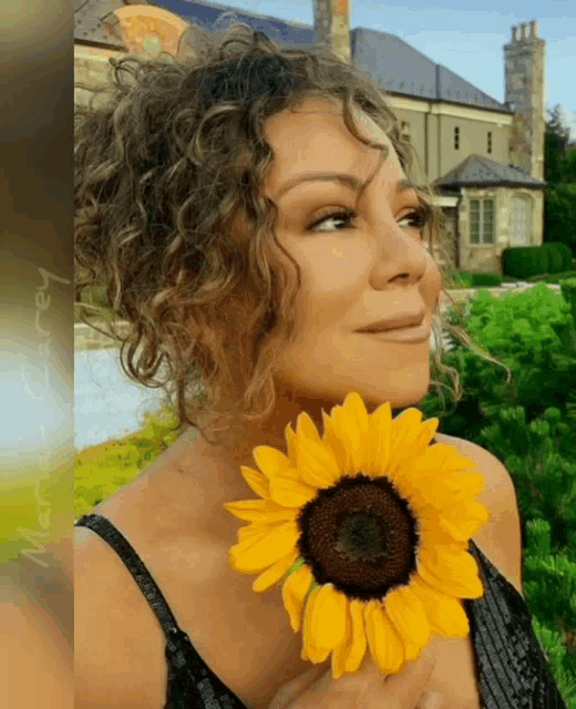 a woman with curly hair is holding a sunflower in her hands