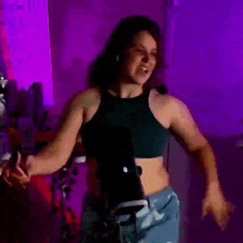 a woman in a crop top and shorts is dancing in front of a purple light .
