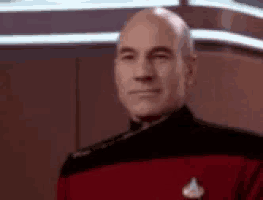 a bald man in a red uniform is standing in a room and smiling .
