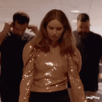 a woman in a sequined top is standing in a hallway with other people .