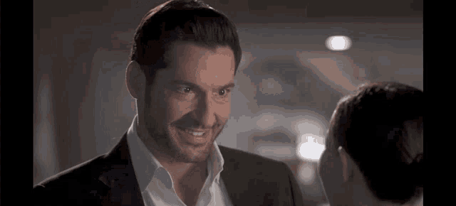 a man in a suit and white shirt is smiling while looking at a woman .