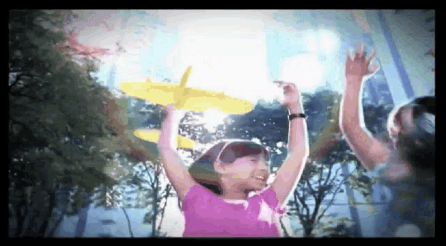 a girl in a pink shirt is holding a yellow toy airplane