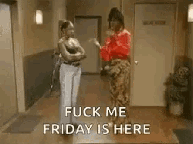 two women are standing next to each other in a hallway and talking .